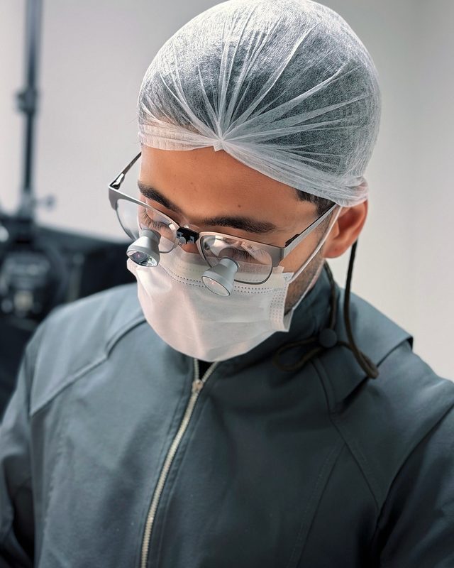 Dentista com lupa cirúrgica e touca.